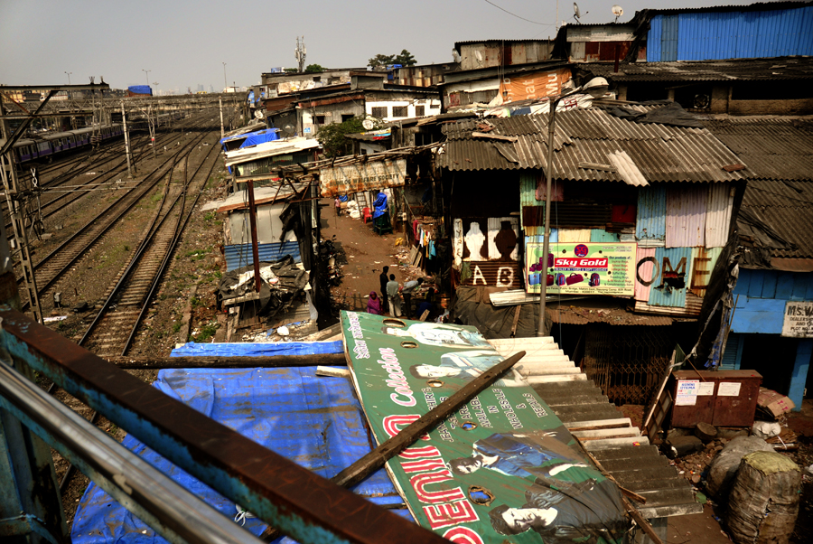 As cities grew, so did the slums, welcoming more rural migrants and creating more urban poverty in India. Even though people keep on flowing from the countryside, the Indian government has persisted in not creating enough housing for everyone. However, things are getting better as proportionally speaking poverty has been waning over the past decade. The photo was taken near the Mahim Station Road in Mumbai, India.