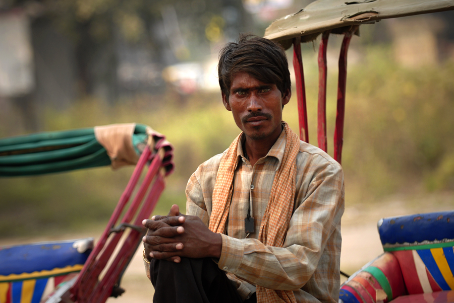 'Wallah' or 'Wala' or 'Vala', derived from Gujarati, Bengali, Marathi or Hindustani, an Indian surname or suffix indicating a person involved in some kind of activity, where they come from or what they wear 'Topiwala'. In this portrait photograph a staring rickshaw wallah has been photographed waiting in his cycle rickshaw in Varanasi in India.